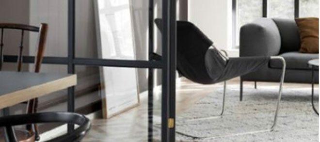 Moderne loungeområde med glasvæg, lænestol og sofa i stilren skandinavisk indretning.