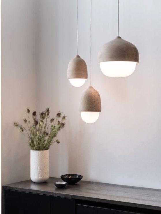 Tre pendellamper i naturmateriale med blødt lys over skænk med vase og tørrede blomster i minimalistisk indretning.