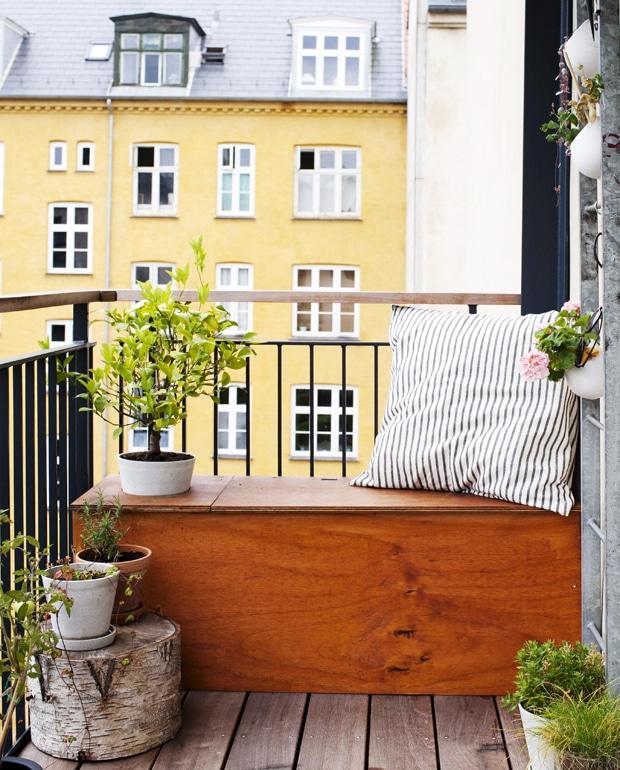 Hyggelig altan med træbænk, puder og grønne planter i skandinavisk boligindretning.