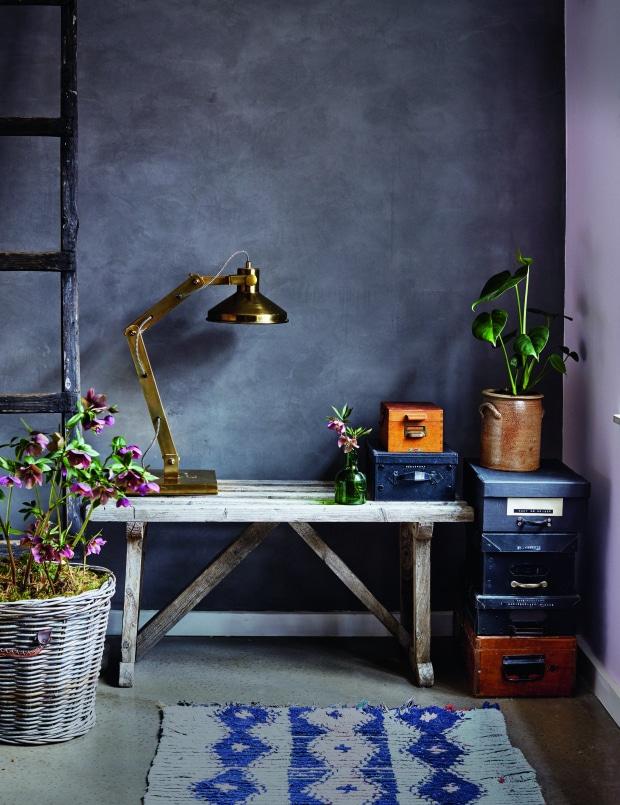 Hyggeligt hjemmekontor med rustikt træbord, messingbordlampe, planter og dekorative opbevaringskasser i stilfuld nordisk indretning.