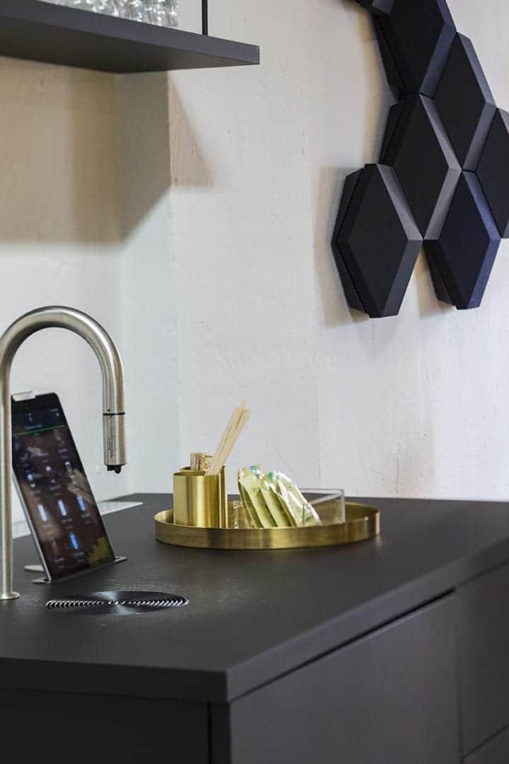 Moderne køkkenbord med sort bordplade, vandhane, tablet og geometriske vægpaneler i stilren skandinavisk indretning.