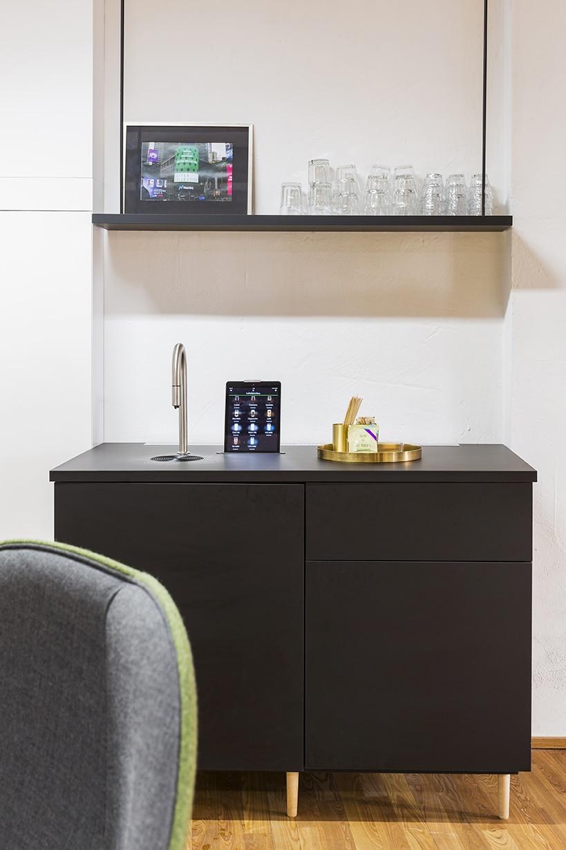 Moderne tekøkken i kontormiljø med sort skab, vandhane, tablet og minimalistisk skandinavisk indretning.