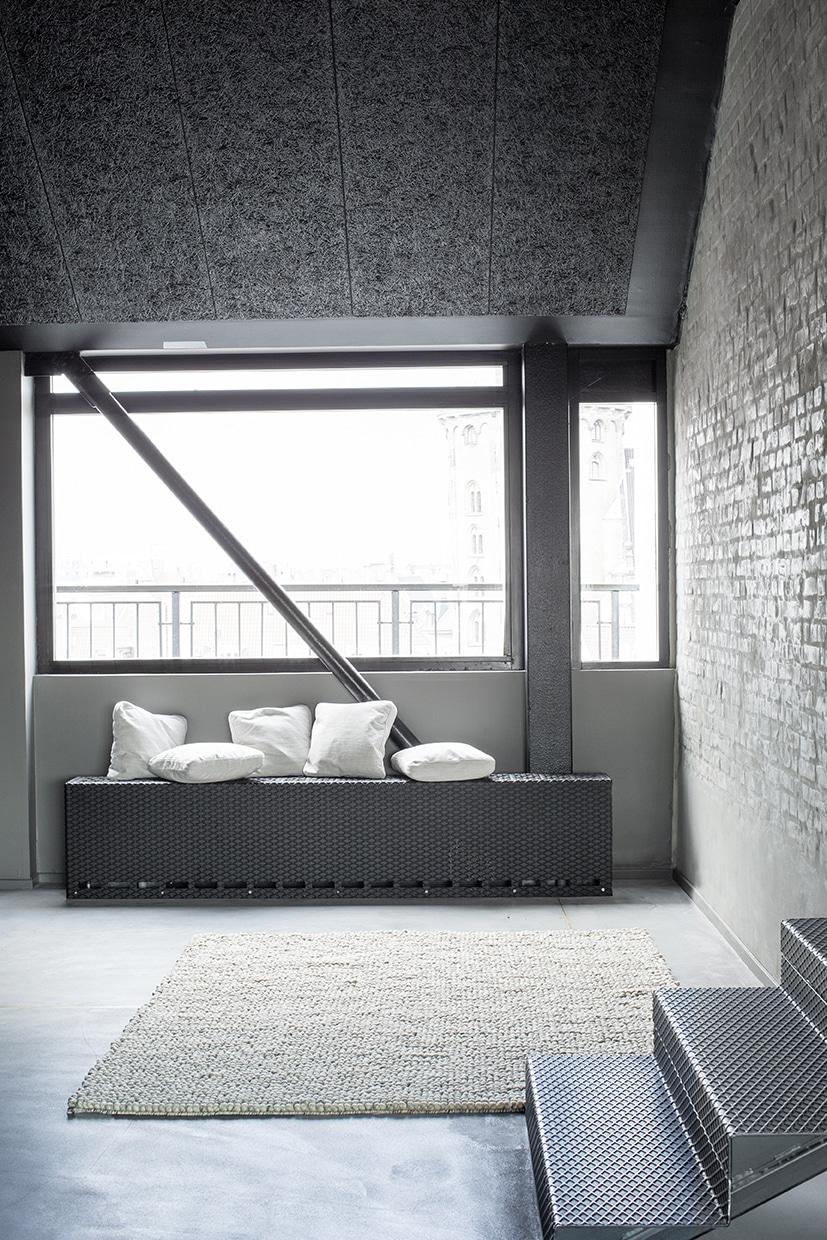 Moderne loungeområde med minimalistisk sofa, store vinduer og rå vægge i stilren skandinavisk indretning.