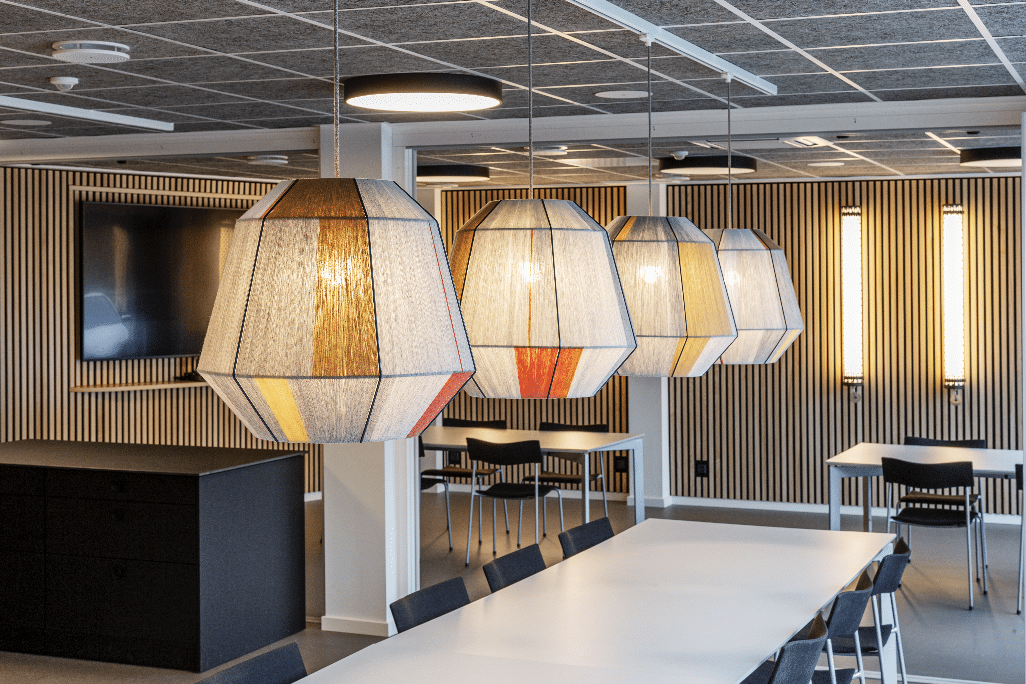 Moderne spise- og mødeområde med store pendellamper, hvide borde og vægge med lodrette trælameller.